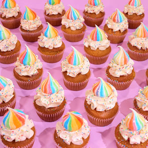 Unicorn Cupcakes by Crumbs & Doilies featuring vanilla sponge with rainbow swirl buttercream and sprinkles on pink background